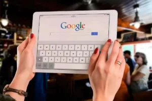 imagem de mãos femininas segurando um tablet com o site do google aberto.